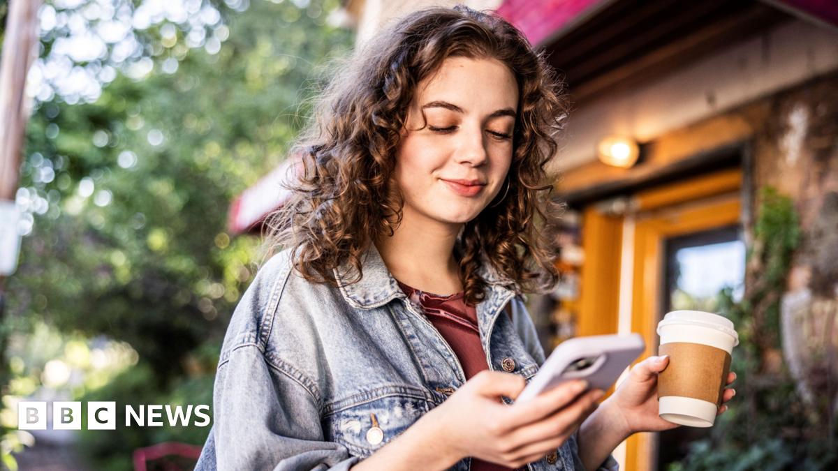 a woman with curly hair holding a coffee looks at her phone
