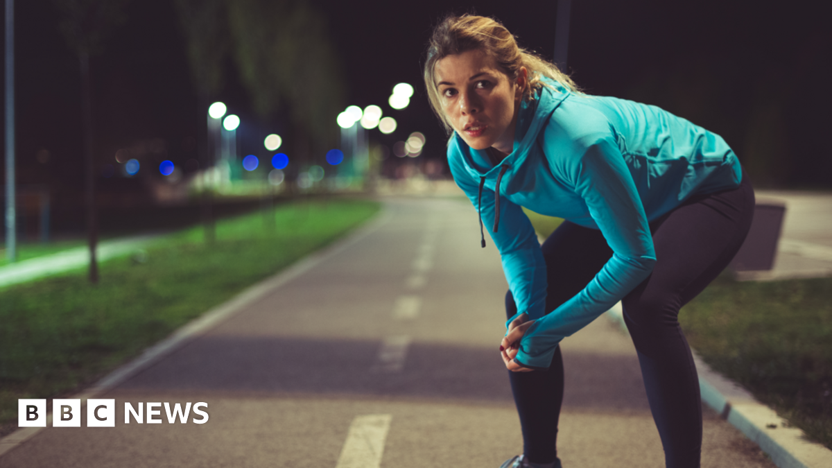 A woman out jogging at night and pausing for a rest 