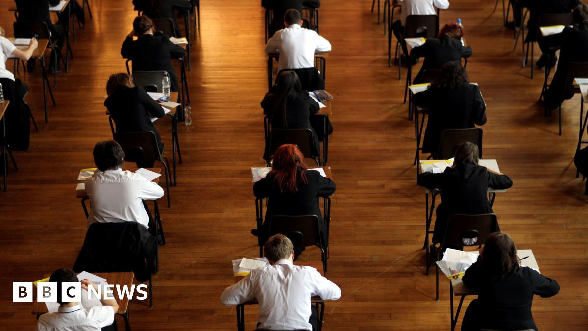 Rows of boys and girls in school uniform sitting at individual tables, appearing to be in the middle of an exam. They are photographed from the back