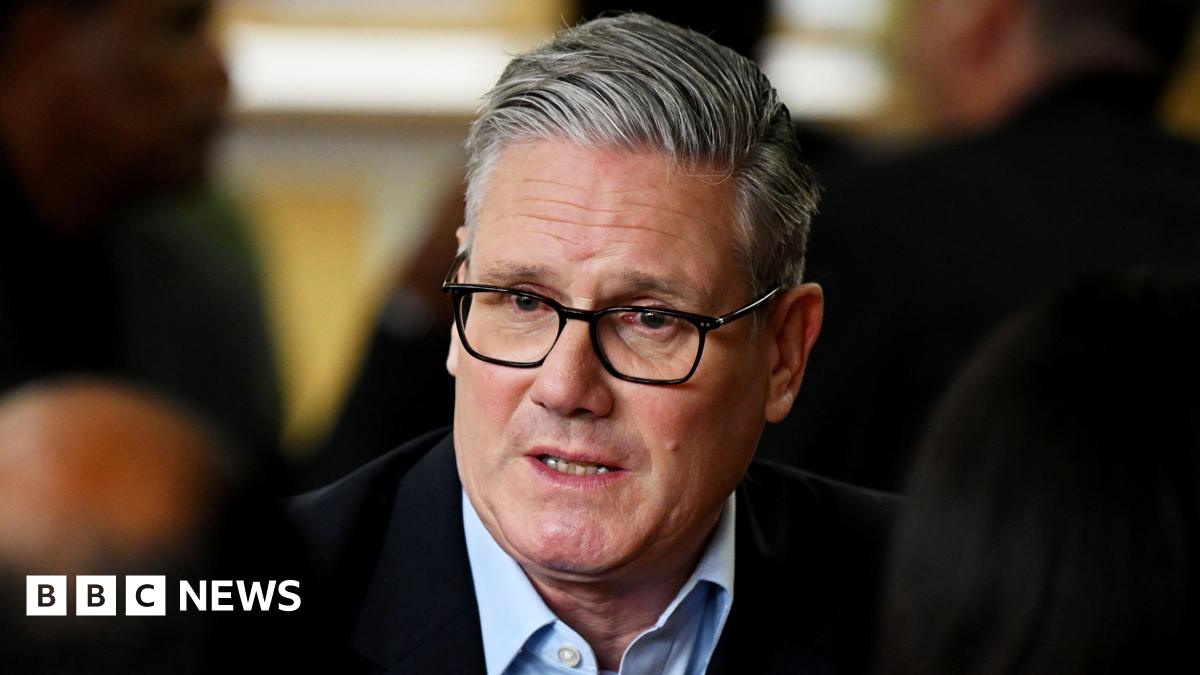 Keir Starmer, in an open neck shirt and suit jacket, looking pensive