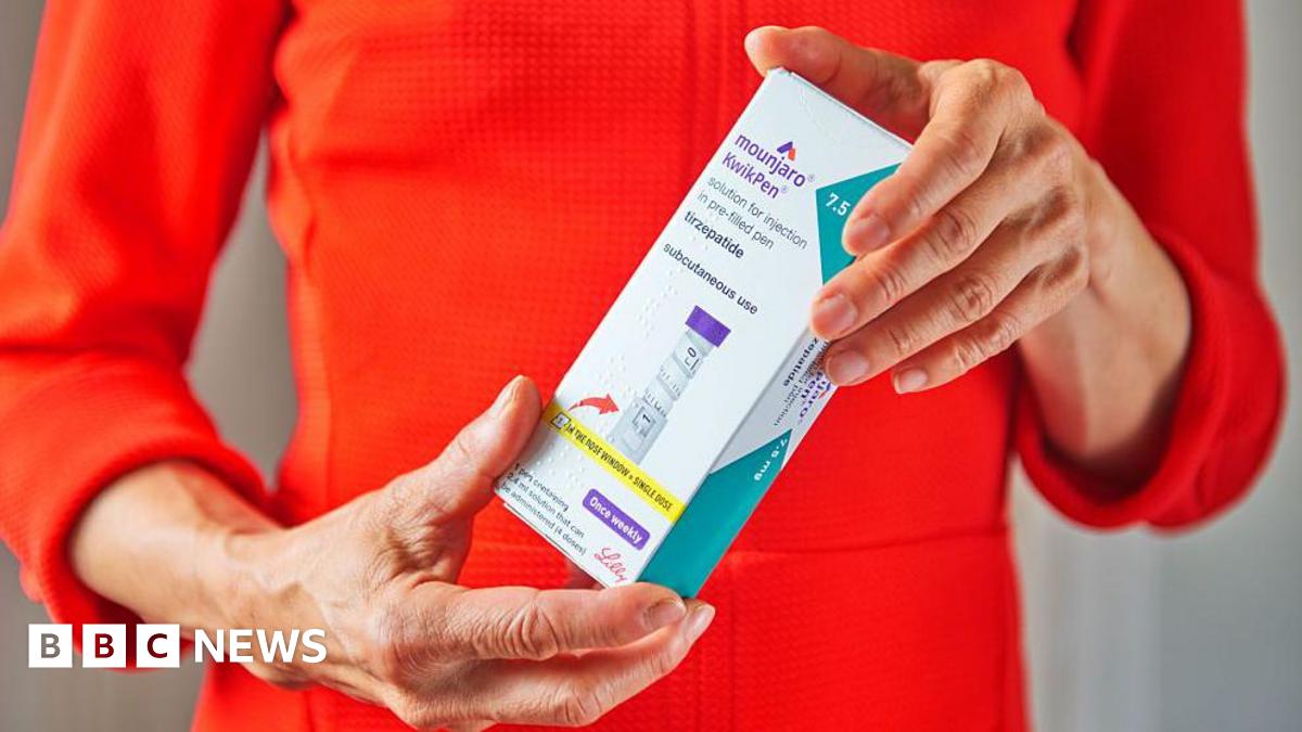 A woman wearing a bright orange top holds a branded box of Mounjaro KwikPen in both hands in front of her - her face is not visible