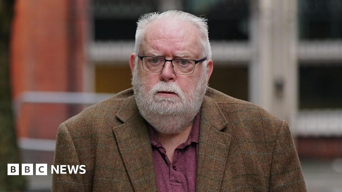 Former Co-op Bank boss Paul Flowers wears a burgundy polo shirt and brown jacket - he has a white beard and hair and is wearing glasses