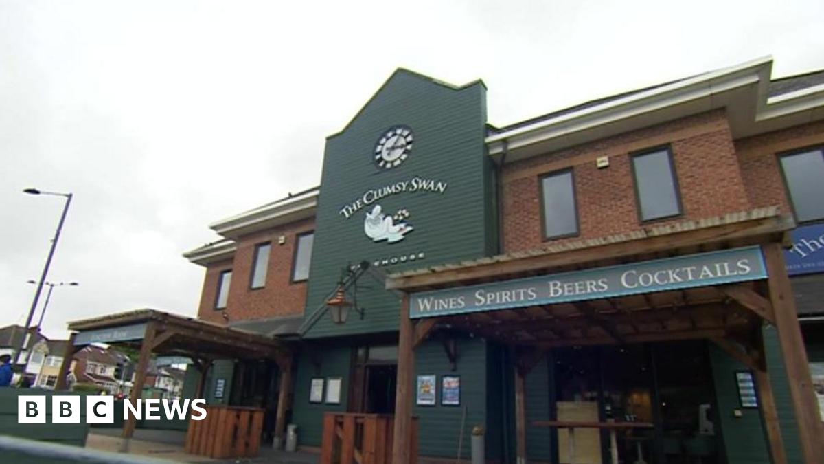 External shot of a brick-built pub with a large green panel featuring a clock and The Clumsy Swan pub sign