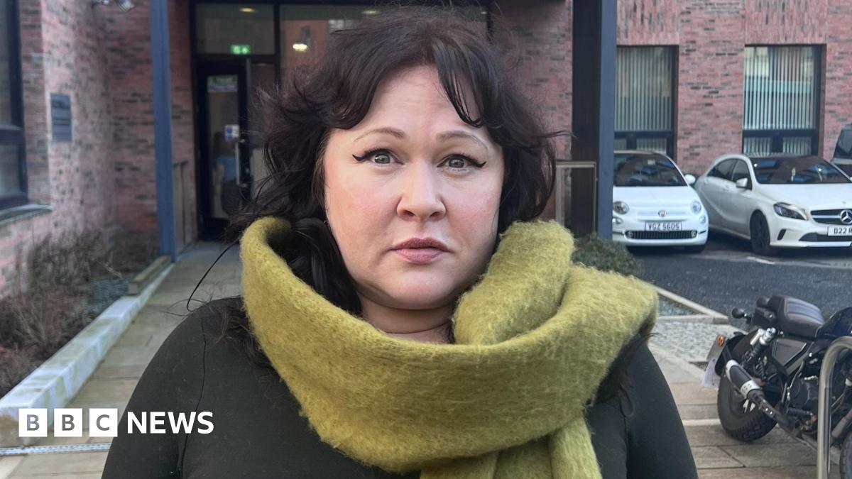 Ms Morrison has dark black hair and is wearing makeup including a winged eyeliner. She has a bright green scarf and a black top.