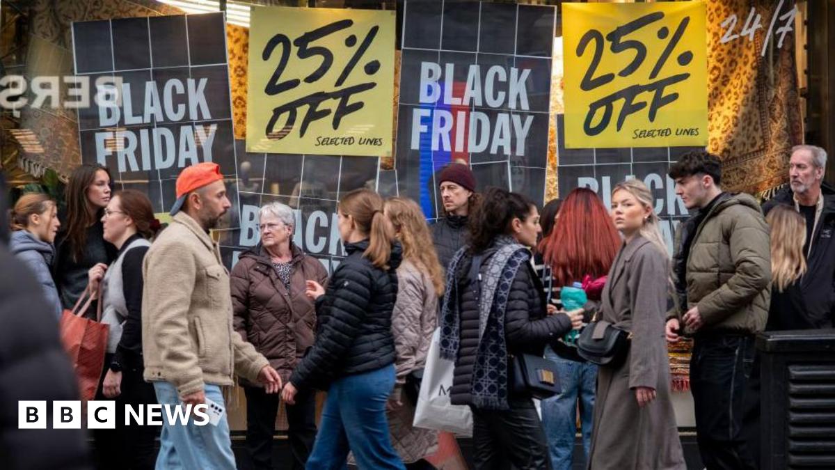 A crowd of people dressed in warm clothing walk along Oxford Street in London, in front of a department store advertising discounts in-store for Black Friday