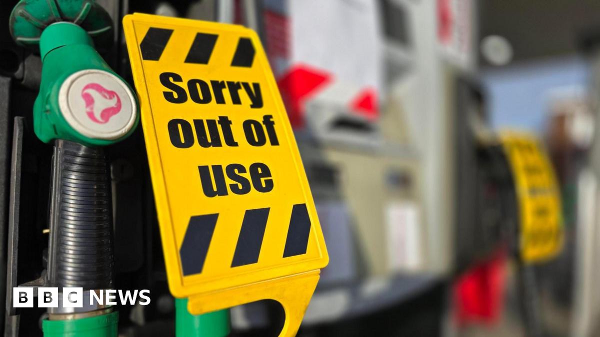 A yellow "sorry out of use" sign over green unleaded petrol pump nozzles.