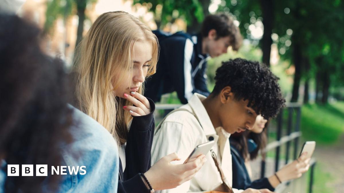 Stock image of three young people looking at their phones in a park.