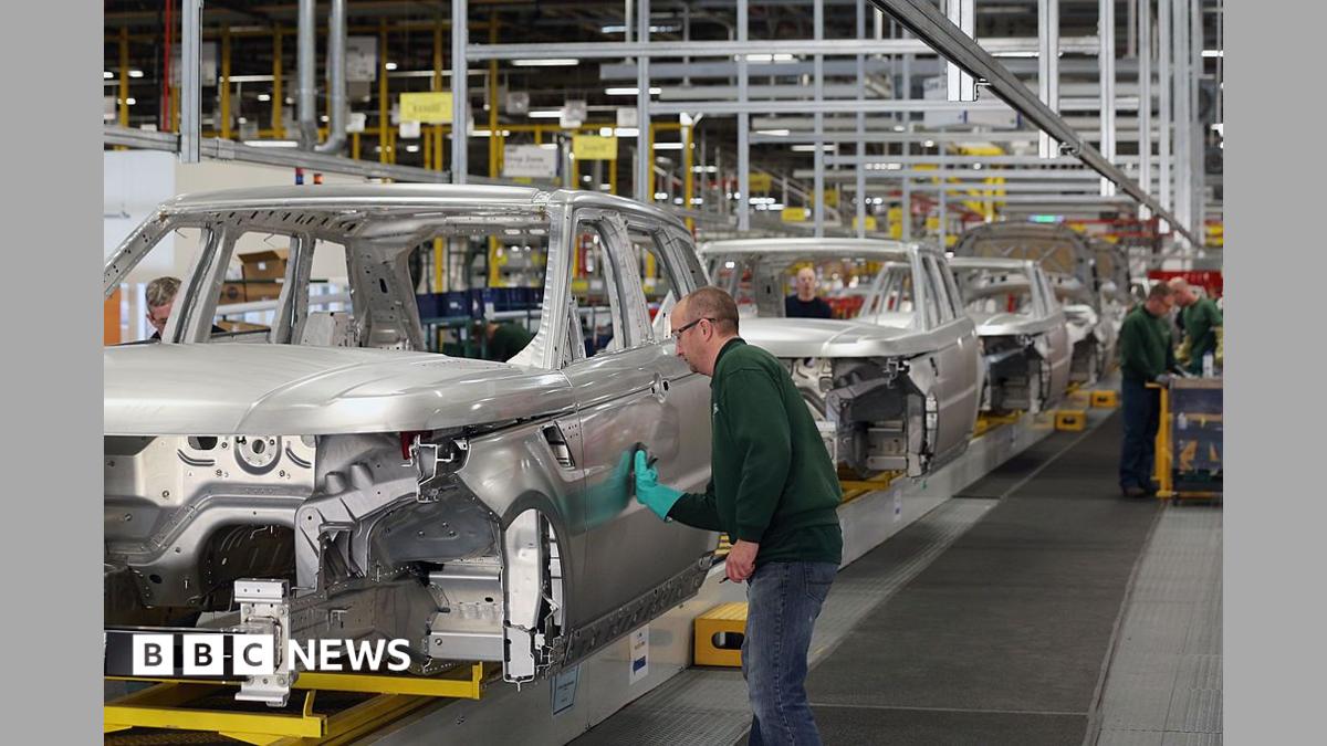 Photo: BBC A factory line of shells of cars- a man wearing a green jumper, safety goggles and a green glove is standing sideways