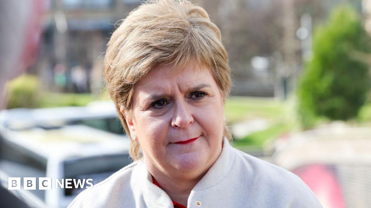 A woman with light-coloured hair photographed outside the Scottish Parliament in a close-up shot. She is wearing a white jacket and is visible from the shoulders up. 