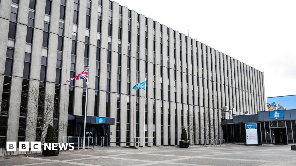 The outside of Darlington Town Hall which is a large, brutalist building with columns of narrow windows. There is a Union Jack flag flying outside the entrance along with another blue flag. 