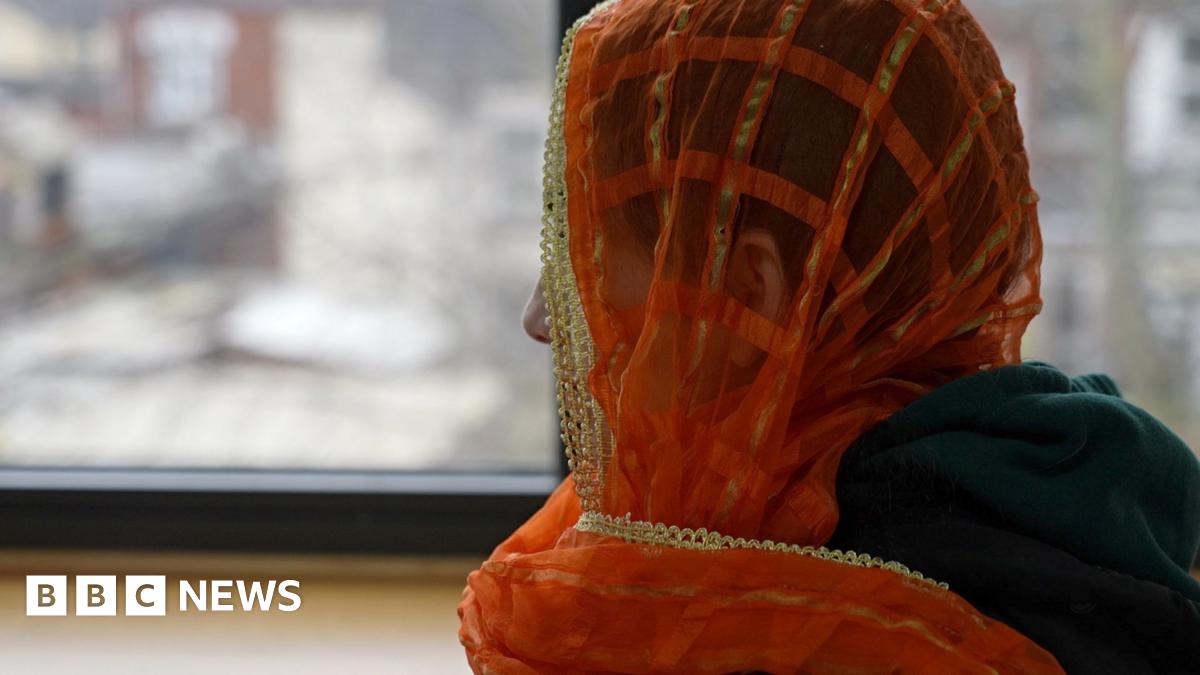 A woman, whose identity cannot be seen, in an orange headscarf looking away from the camera