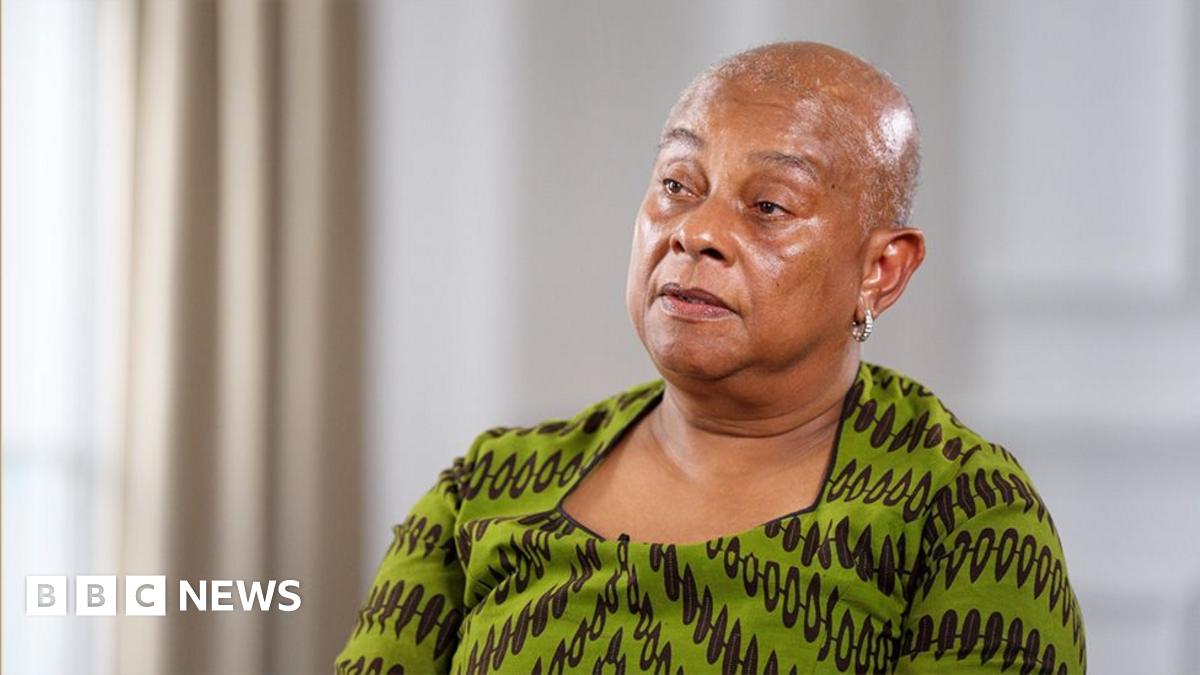Doreen Lawrence wears a green dress with black patterning, and is sitting in a large formal room