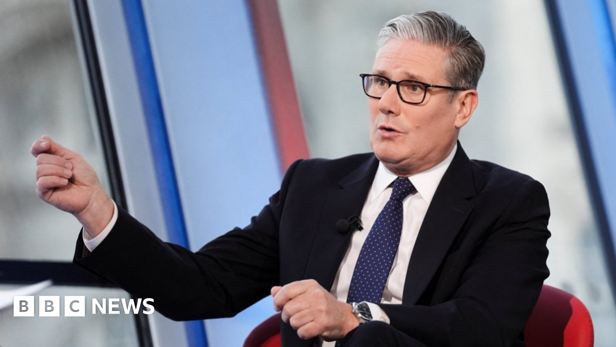 Sir Keir Starmer speaking to the BBC. He is wearing a black suit, with a white shirt and blue patterned tie. He is also wearing dark glasses and gesturing with his hand.