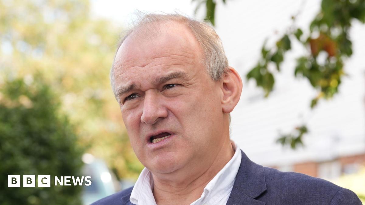 Sir Ed Davey has open collar and black suit on. He is looking afar. He has grey hair on the sides of his head, which is thin on top.