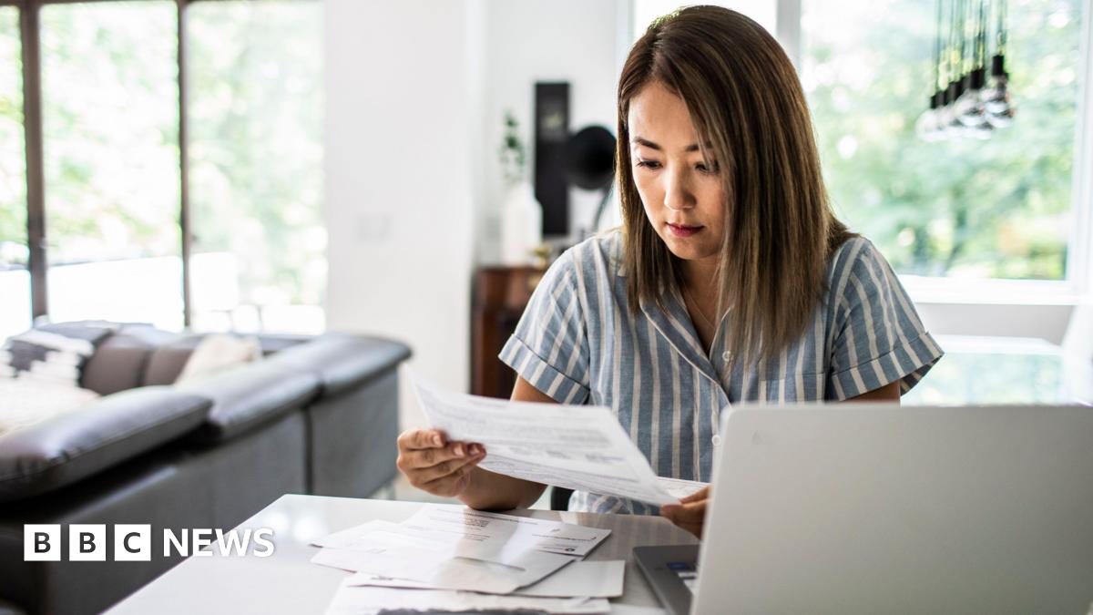 A woman looks at her bills while sat in her living room
