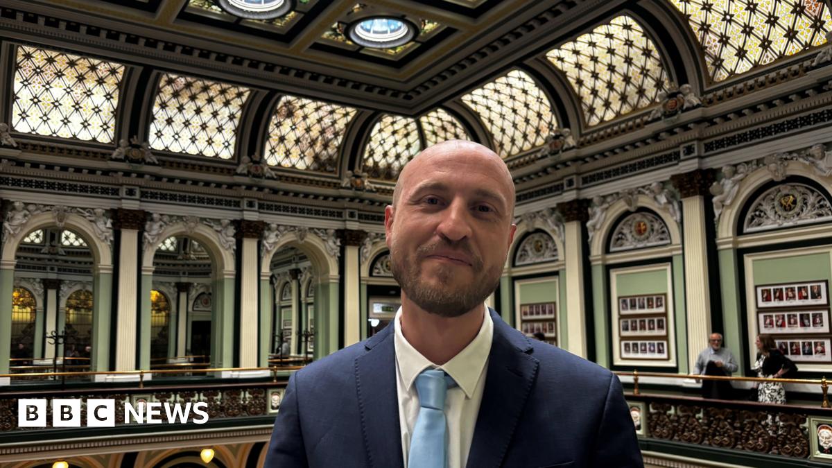 A man in a suit stands inside a council chamber