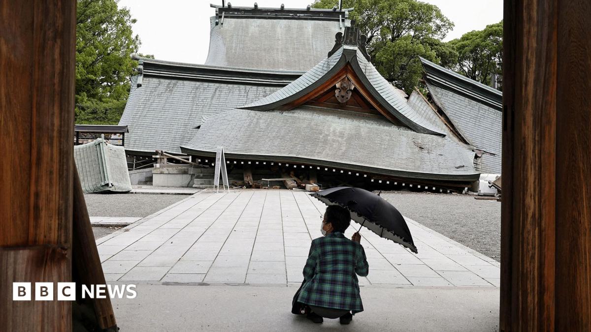 A woman with an umbrella squats in front of a collapsed shrine on Wednesday in Yatsushiro