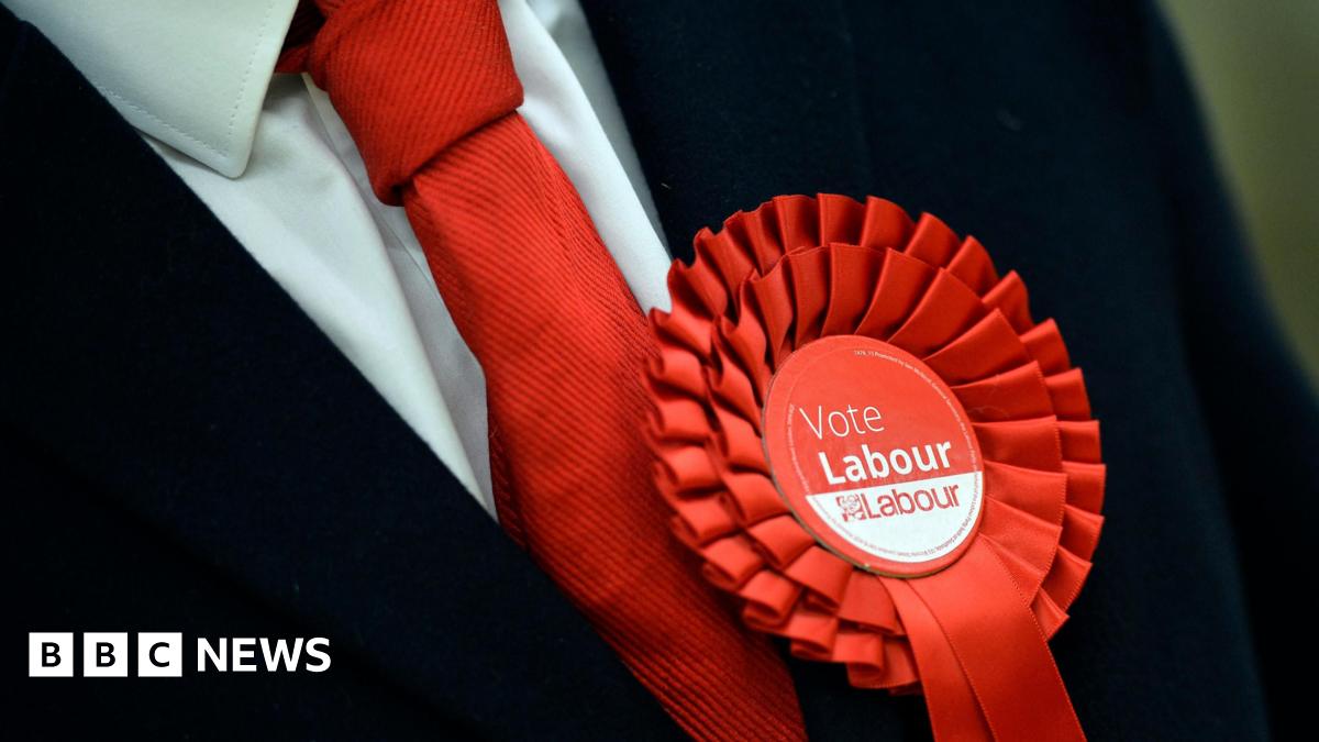 A man with a red tie wearing a red rosette reading 'Vote Labour'