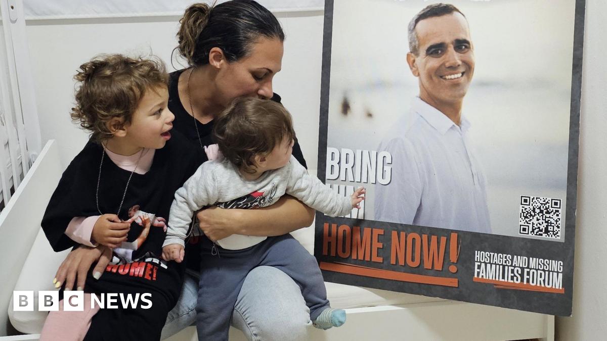 Lishay and her two young daughers sit next to a large photo of Omri Miran