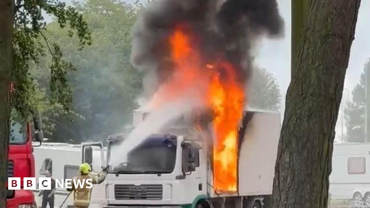 A large white van on fire - huge orange flames a pouring out of the vehicle.