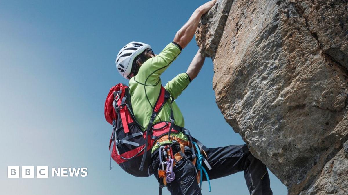 Stock image of a female climber wearing a backpack hanging onto a rock
