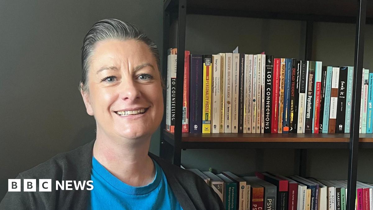 Zoe Hughes, an Exeter City council member, wearing a blue T-shirt and a black top, sitting next to a bookshelf