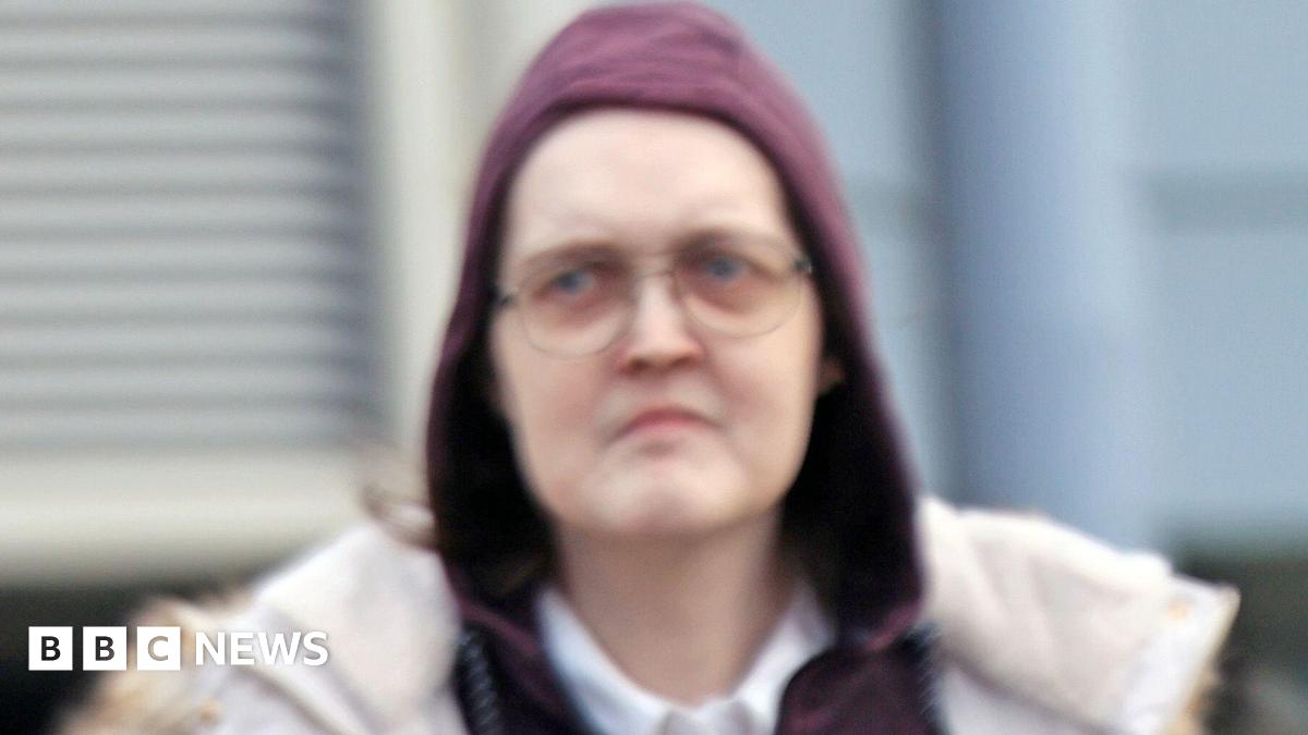 A transgender woman, with a stern expression wearing glasses and a burgundy hoodie which is covering her head.