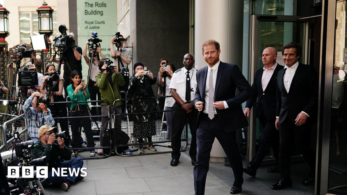Prince Harry leaves the court during his hacking case against the Daily Mirror. He wears a dark coloured suit, white shirt and tie. His barrister David Sherborne, also dressed in a dark suit is on his left.  A crowd of photographers are behind a metal...