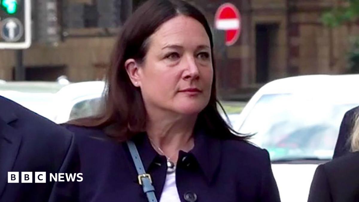 A woman arrives at court wearing a black coat and white top,  she has mid length dark brown hair