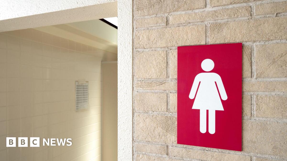 A generic photo of a ladies' toilet sign on a wall outside a toilet. The sign has a white lady symbol on a red background. The doorway has pale cream tiles.