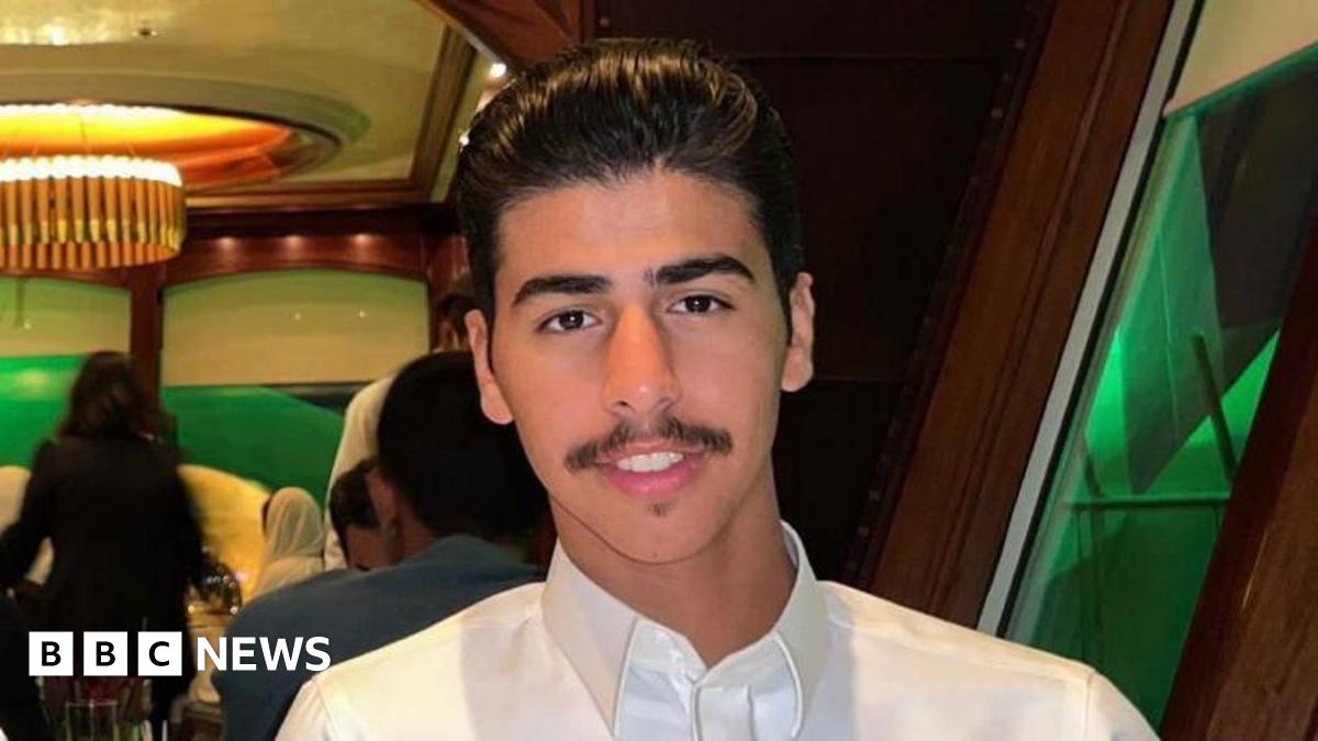 Mohammed Algasim has black hair combed back and a moustache. He is wearing a white shirt and smiling while sitting at a restaurant table.