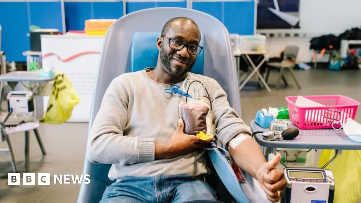 A man is pictured seated while donating blood. He is giving the thumbs up. 
