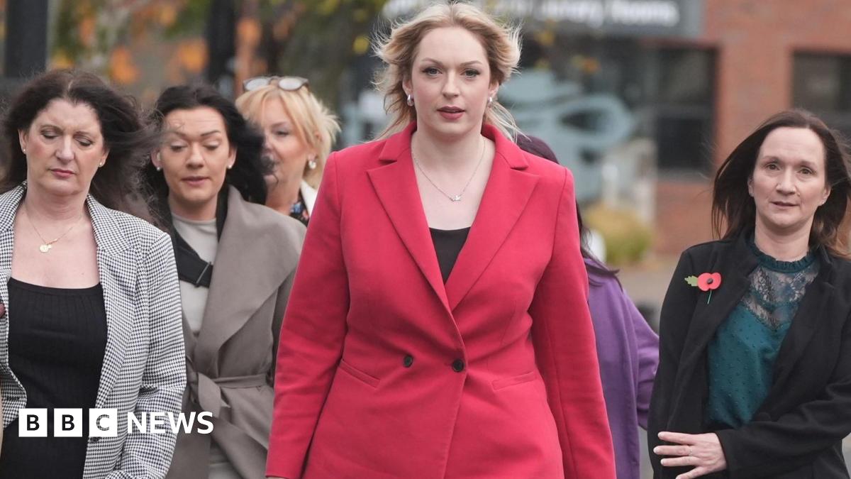 A group of women arrive at the tribunal office. At the head of the group is Bethany Hutchison, who has long blond hair and is wearing a red coat. Beside her are several smartly dressed women with long brown hair.