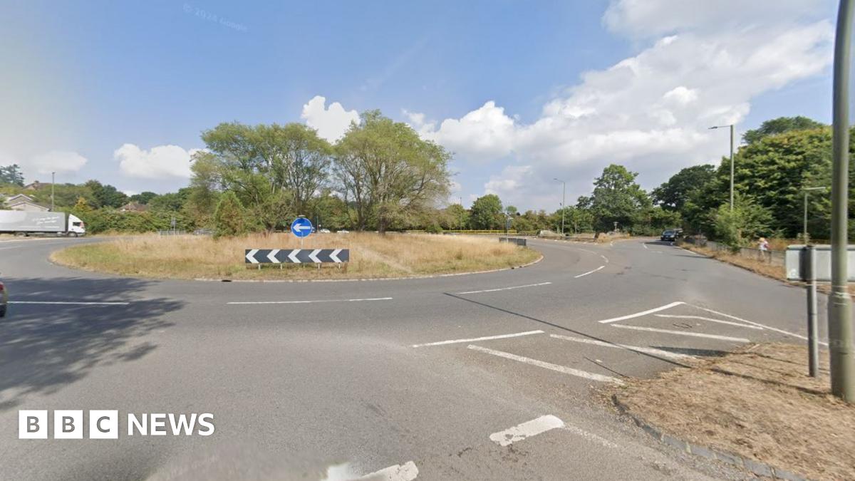 A Google Maps image of a roundabout. There is a lorry to the left of the road and a car approaching from the right. 