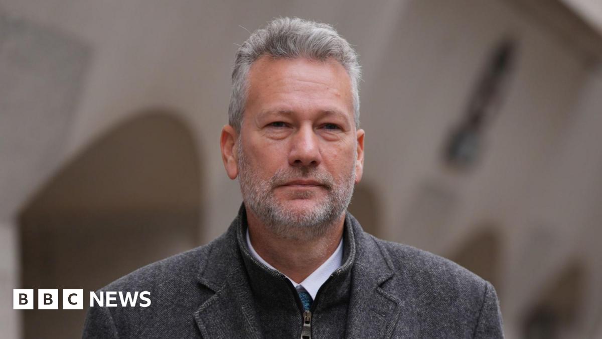 Nathan Gill; a man with a grey coat on, and underneath there is a turquoise tie and white shirt. He has short grey spiked hair and a a grey beard.