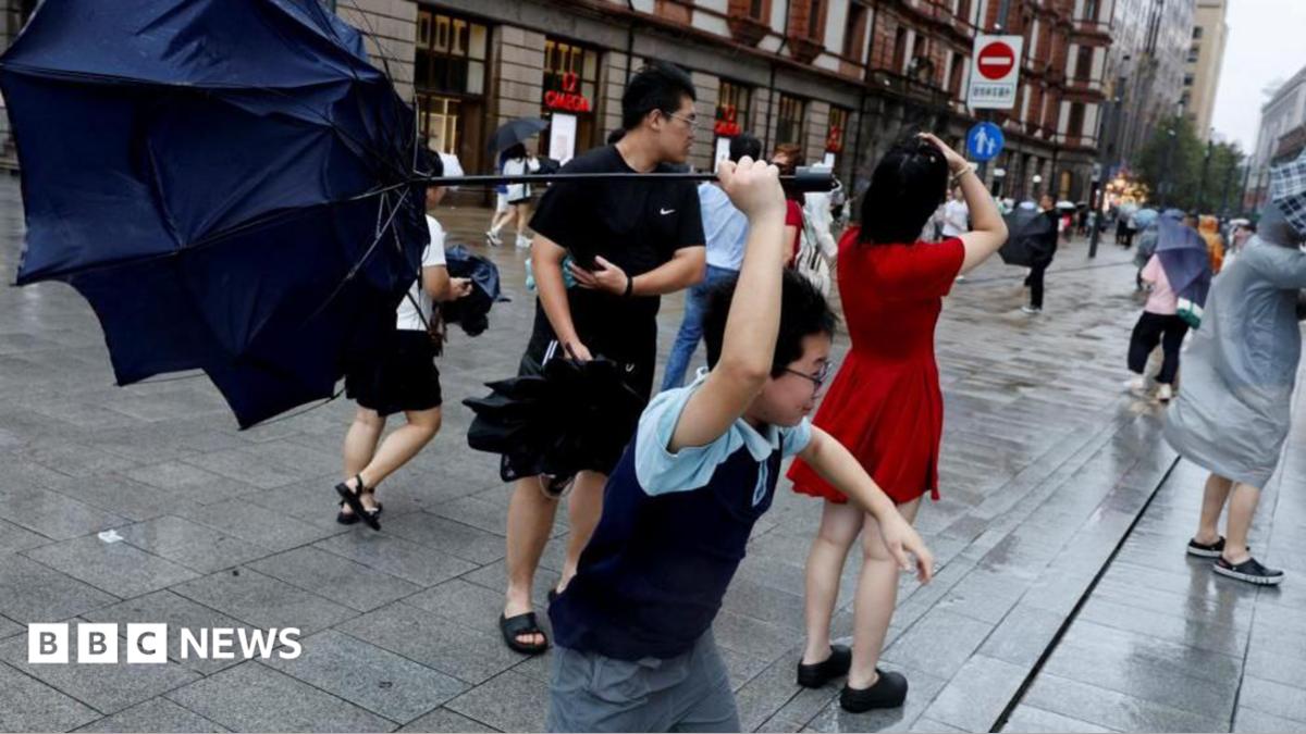 People holding umbrellas along a street in Shanghai. One boy is seen trying to hold on to an inverted umbrella as winds