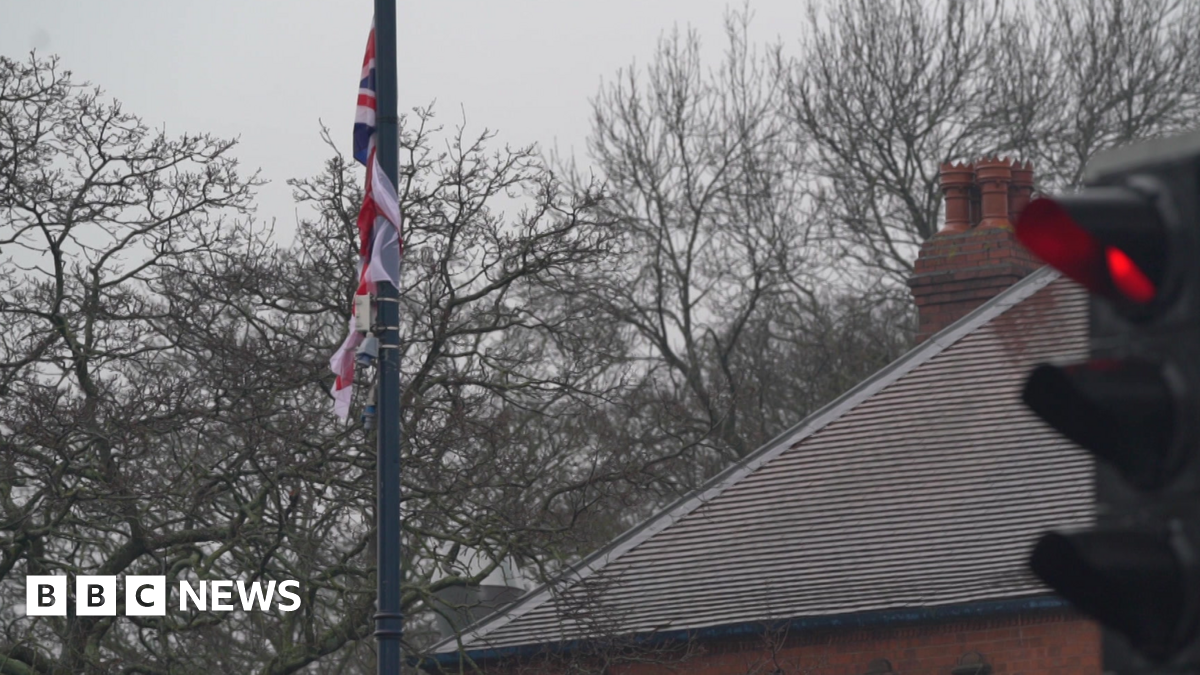 A union jack is attached to a flag pole. A sloping roof can be seen on the right with a traffic light in the foreground