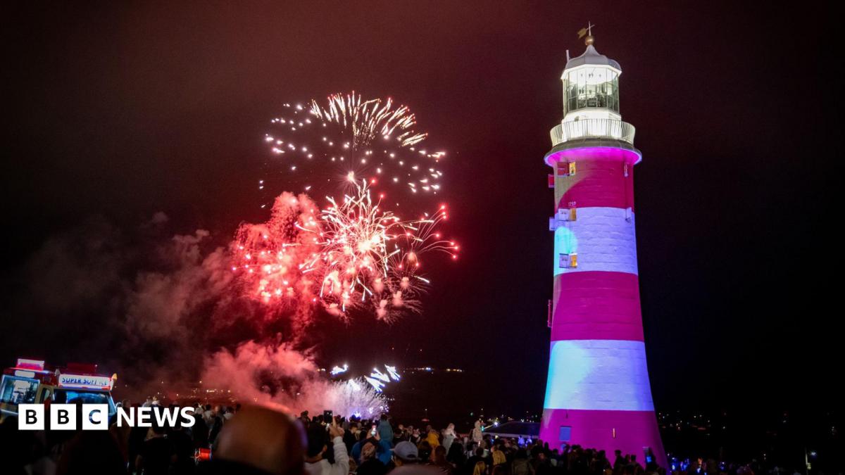 Photo: BBC A number of fireworks explode behind Smeaton's Tower. The tower is red and white striped with a lantern at the top