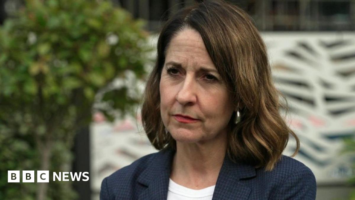 A medium close up of Pensions Secretary Liz Kendall wearing a blue jacket and white top with tree and bushes in background