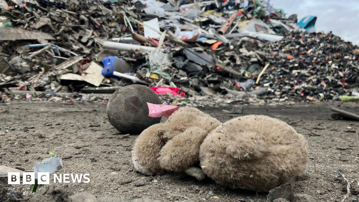 A soft toy and ball lying in front of a large pile of rubbish