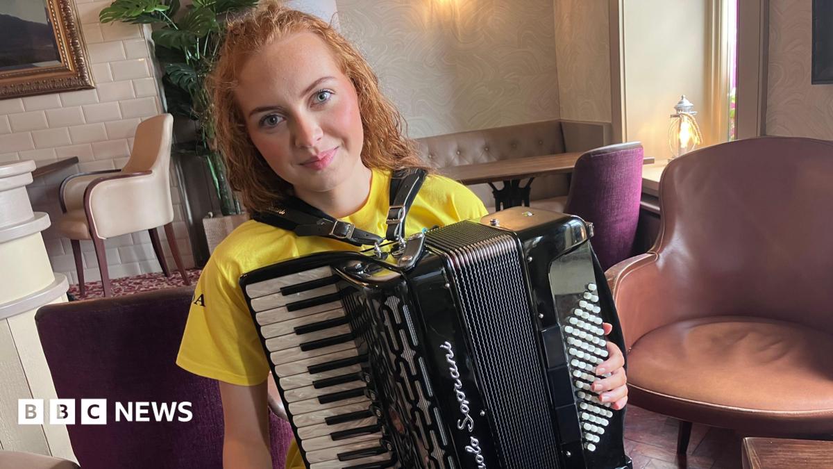Photo: BBC A young woman is holding an accordion. She's sitting in an empty restaurant