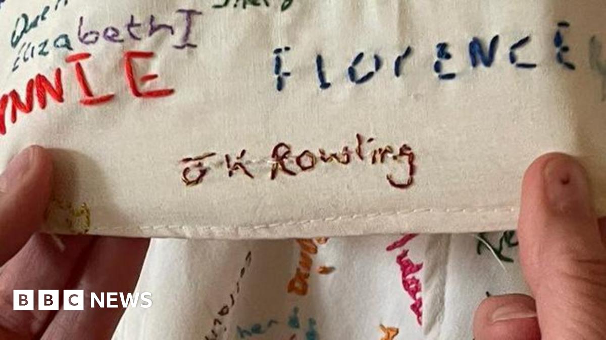 A pair of hands are holding a piece of fabric covered in embroided names. The one being held prominently to the camera is "JK Rowling"