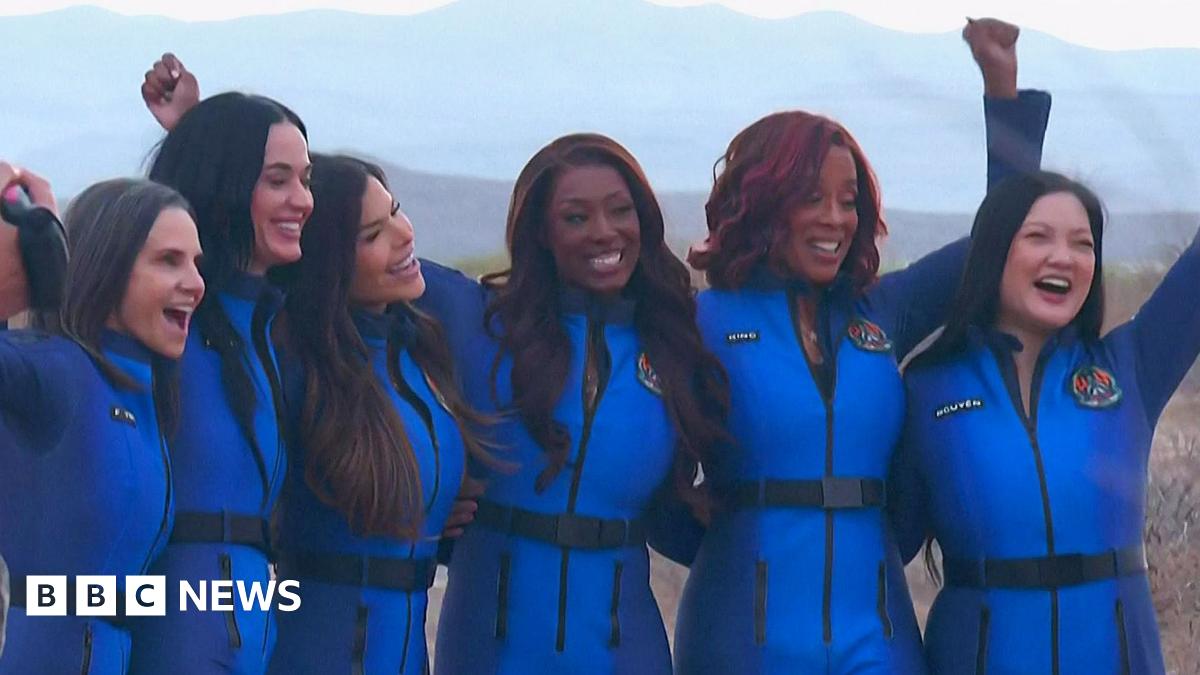 The Blue Origin crew lock arms and cheer after landing back to earth with mountains in the background