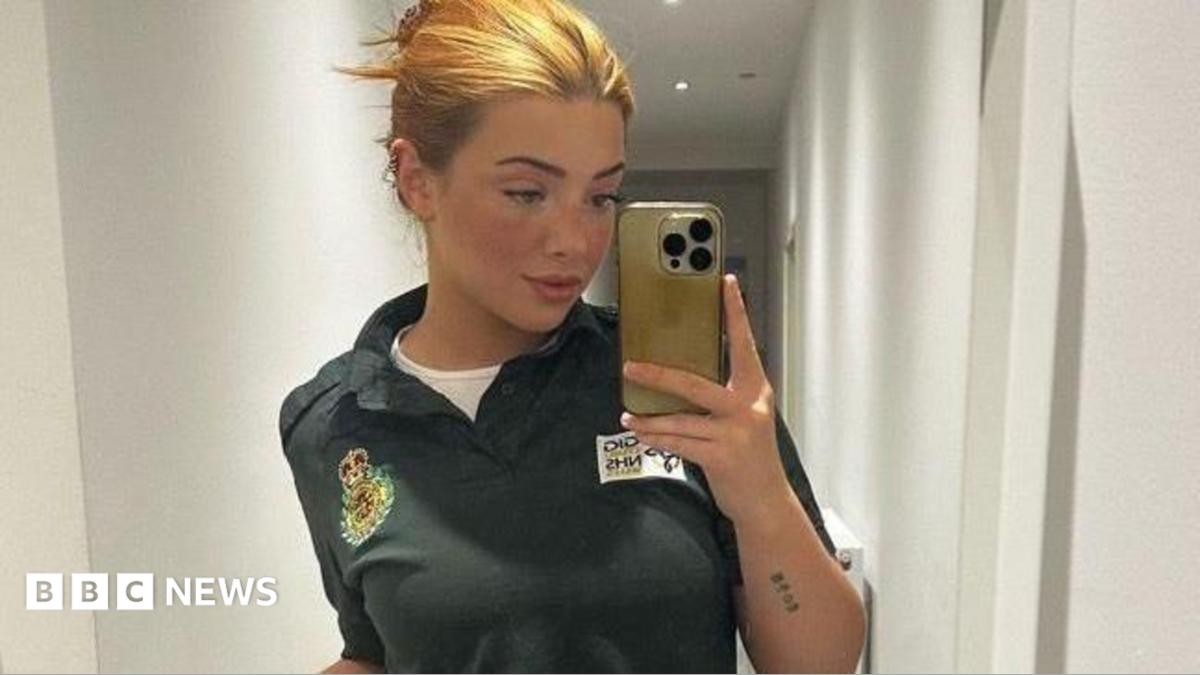 Lorna is using her mobile phone to take a selfie in a mirror here. She has blonde/ginger hair which is pinned up. She's wearing a green Welsh ambulance service polo shirt with a white shirt underneath. 