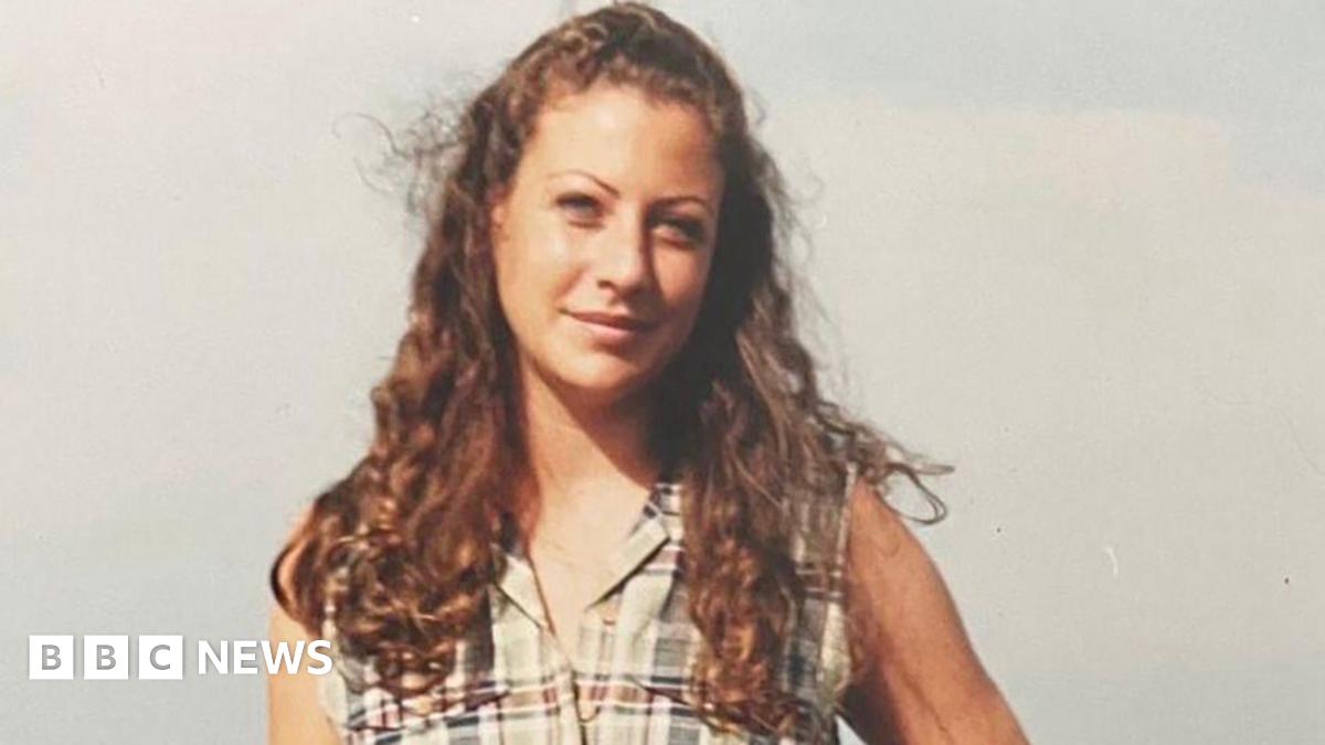 A photo of a young woman with long auburn curly hair wearing a pale checked sleeveless top