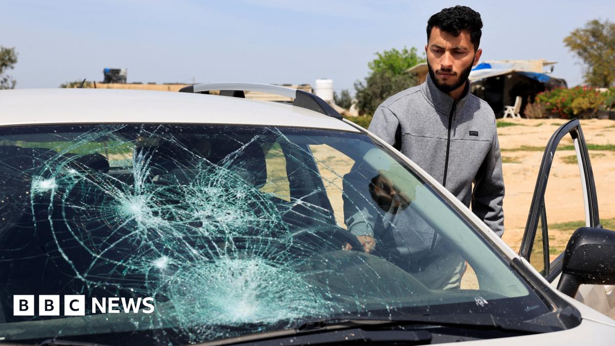 Basel Adra looks at a grey car with its window smashed.