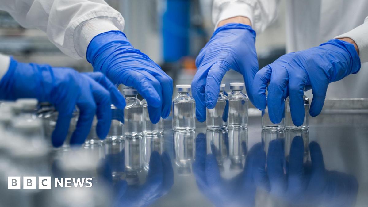 Blue gloved hands in a lab picking up vials of clear liquid