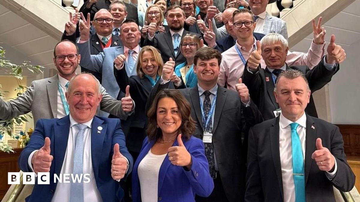 Reform UK members of Kent County Council with their thumbs up. They are stood on stairs. 
