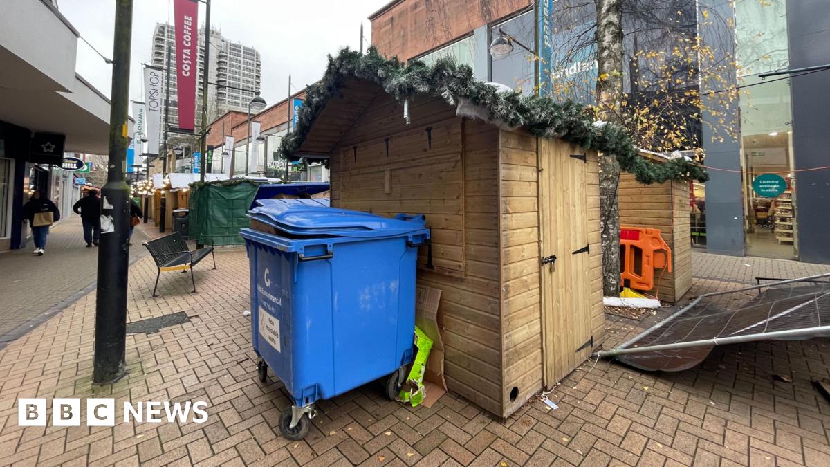 A large blue wheelie bin stands in front of a closed wooden stall at Swindon Christmas market