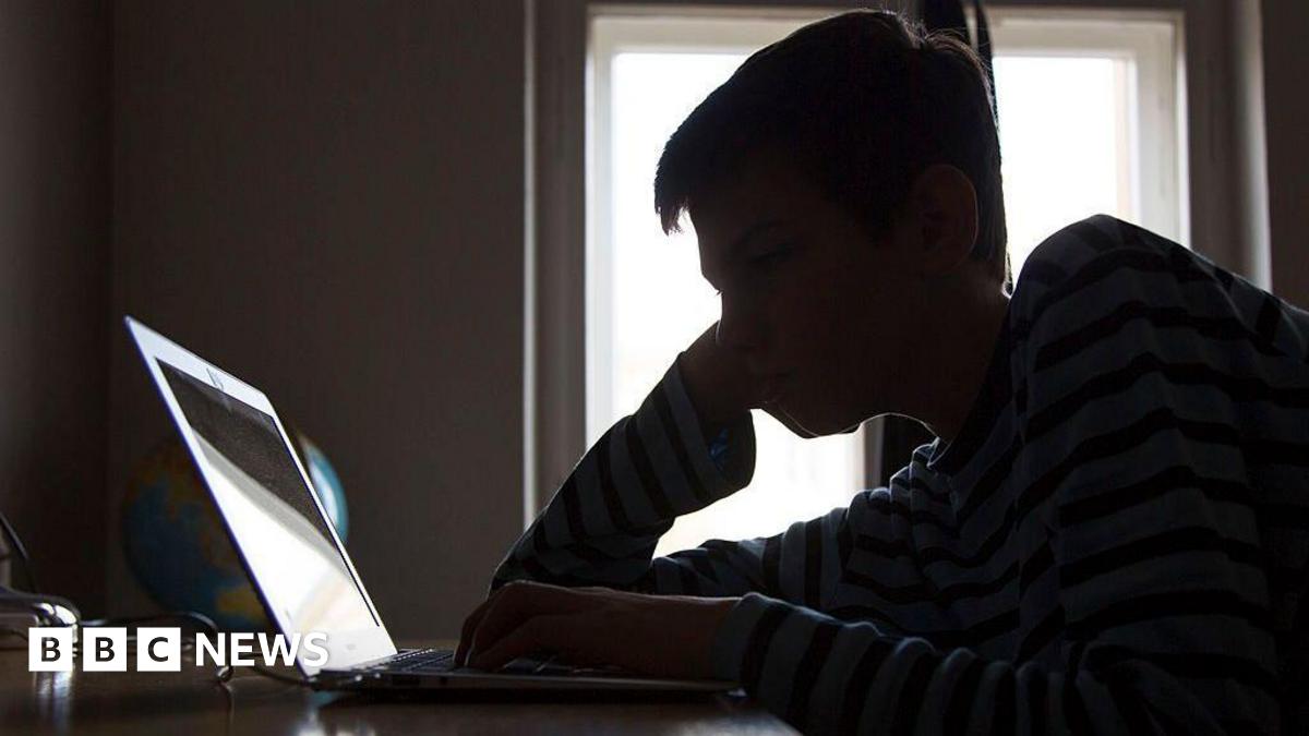 A silhouette of a boy reading the screen of a laptop